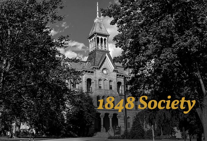 Old Main surrounded by trees with 1848 Society Logo